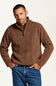 A man wearing a brown quarter-zip fleece pullover sweater with a mock neck, paired with blue jeans, standing against a plain off-white background.