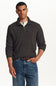 A man wearing a dark charcoal gray ribbed quarter-zip sweater over a white collared shirt and blue jeans, standing against a plain white studio background.
