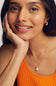 A close-up lifestyle shot of a woman wearing a delicate gold chain necklace with a small cream-colored ghost pendant, styled with a bright orange ribbed tank top.