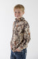 A young boy with short blonde hair smiling and standing at a three-quarter angle, wearing a long-sleeve quarter-zip pullover in Leaf Camo with his hands in the pockets of his blue jeans against a plain white background.