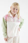 A young girl with blonde hair posing in a fleece quarter-zip pullover featuring an ivory plush body, sage green sleeves, and a pink floral quilt-patterned yoke across the chest and collar, set against a plain light background.