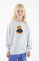 A young blonde girl wearing a light gray heather crewneck sweatshirt with a teddy bear graphic on the chest, paired with blue pants, photographed against a clean white background.