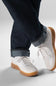 White sneakers with brown soles worn with dark jeans on a light gray background