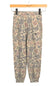 A pair of jogger-style pants with an abstract organic camouflage pattern in beige, brown, and gray, hanging from a wooden hanger against a white background.
