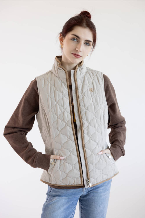 A woman modeling a quilted zip-front vest over a brown long-sleeve shirt and blue jeans, photographed against a plain light background.