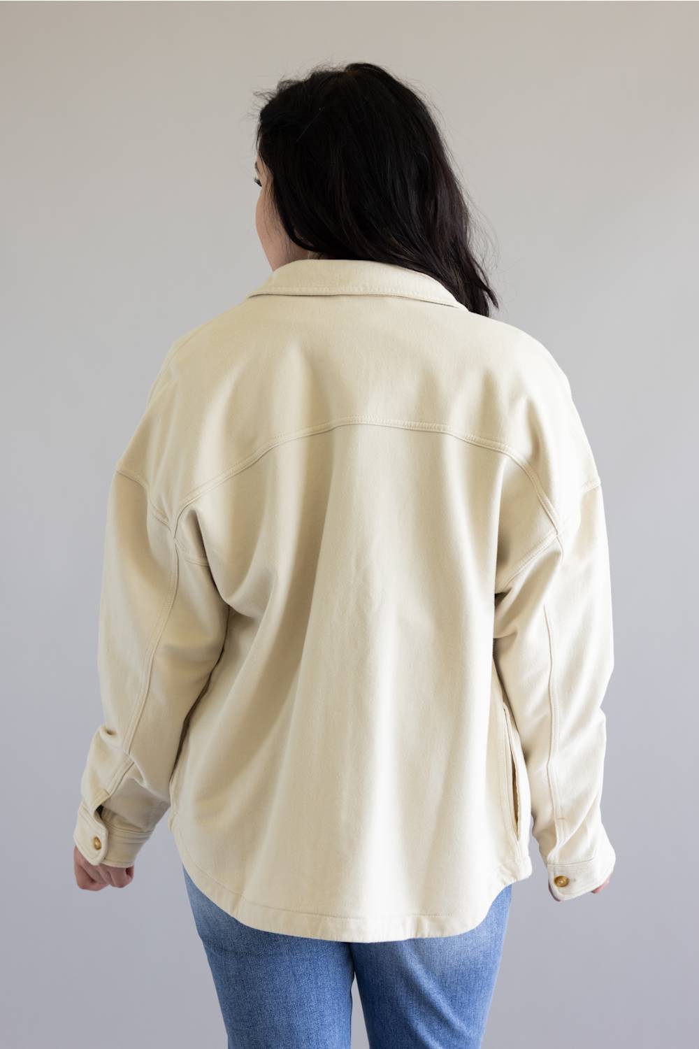 Person wearing a beige jacket and blue jeans against a plain background