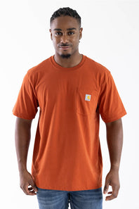 A man wearing a bright orange short-sleeve crewneck t-shirt with a left chest pocket featuring a small Carhartt logo, paired with blue jeans, against a plain white background.