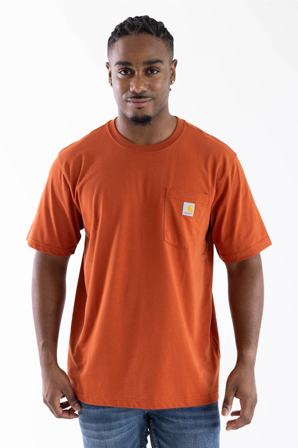 A man wearing a bright orange short-sleeve crewneck t-shirt with a left chest pocket featuring a small Carhartt logo, paired with blue jeans, against a plain white background.