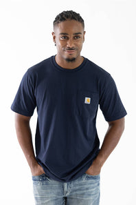 A man wearing a navy blue short-sleeve pocket t-shirt with a small Carhartt logo on the chest pocket, paired with light blue jeans, against a plain white background.