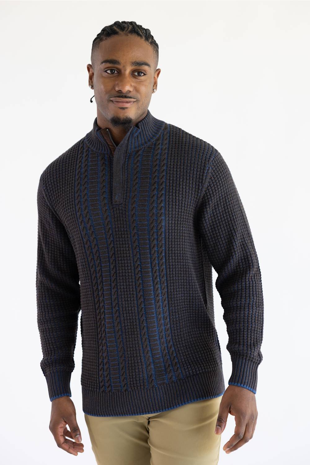 A man wearing a dark brown textured knit mock-neck sweater with vertical blue and white stripe patterns, paired with beige trousers, against a plain white background.