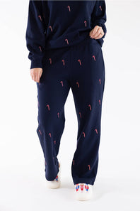 Front view of a woman wearing a navy blue crewneck fleece sweatshirt and matching straight-leg sweatpants, both featuring an all-over embroidered red and white candy cane pattern, finished with white slippers.