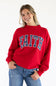 Front view of a smiling woman wearing the red 1897 Active Faith mock neck sweatshirt with navy blue "FAITH" applique lettering filled with white polka dots, paired with blue jeans against a plain white background.