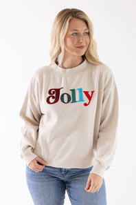 A smiling blond woman wearing a beige crewneck sweatshirt featuring multicolored chenille patch lettering that reads "Jolly" on the front.
