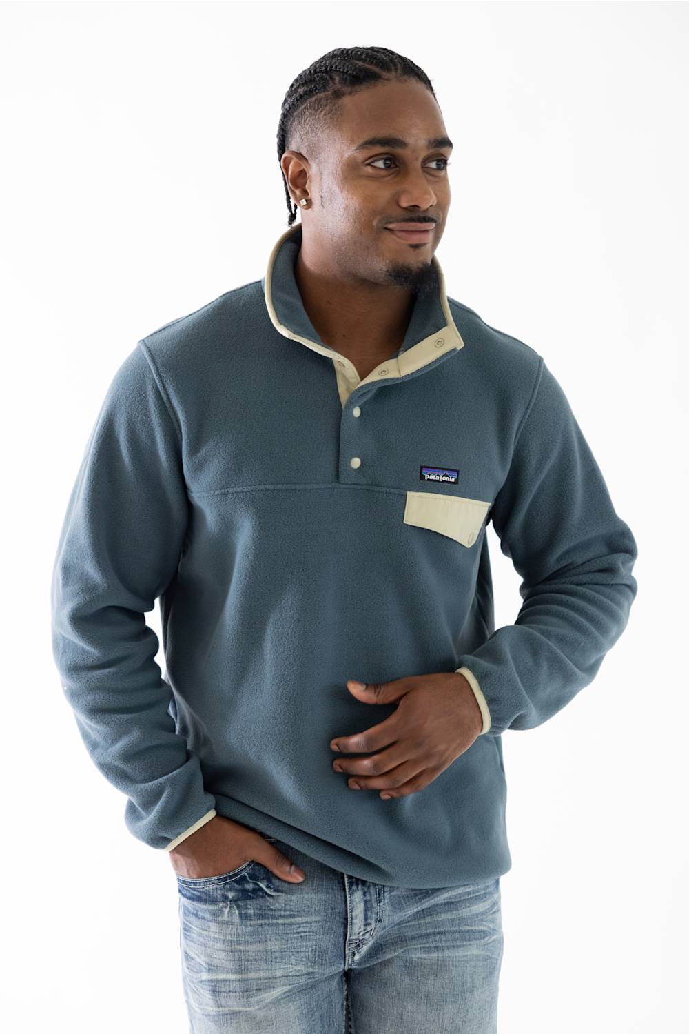 A man wearing a Patagonia fleece pullover in slate blue with beige contrast trim and a chest pocket, paired with blue jeans, against a plain white background.