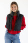 A woman wearing a black quilted puffer vest over a red long-sleeve top and blue jeans, photographed against a plain white studio background.