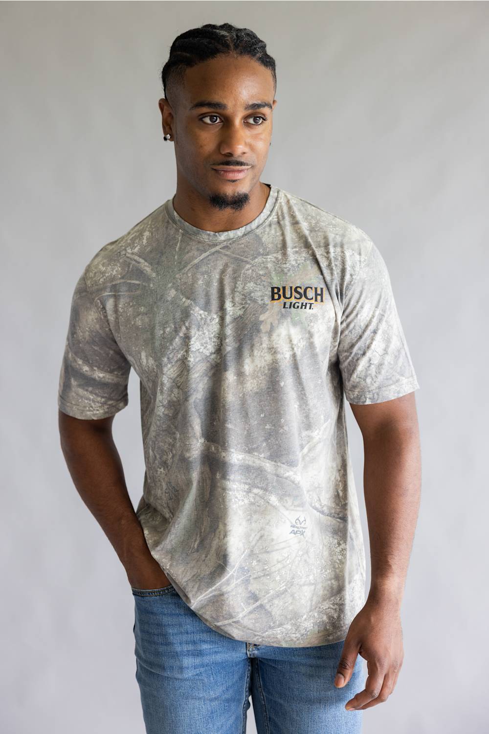 A man wearing a light gray and white camouflage patterned t-shirt with 'BUSCH LIGHT' printed on the chest, paired with blue jeans, standing against a neutral gray background.
