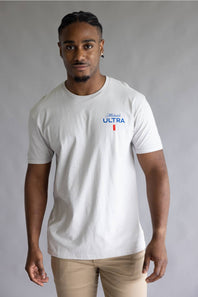 A man wearing a white short-sleeve crewneck t-shirt with a blue and red 'Michael ULTRA' logo on the left chest, paired with beige pants, against a neutral gray studio background.