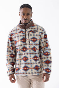 A man wearing a long-sleeve quarter-zip fleece pullover with a Southwestern geometric pattern in red, blue, and beige, paired with beige pants, against a plain white studio background.