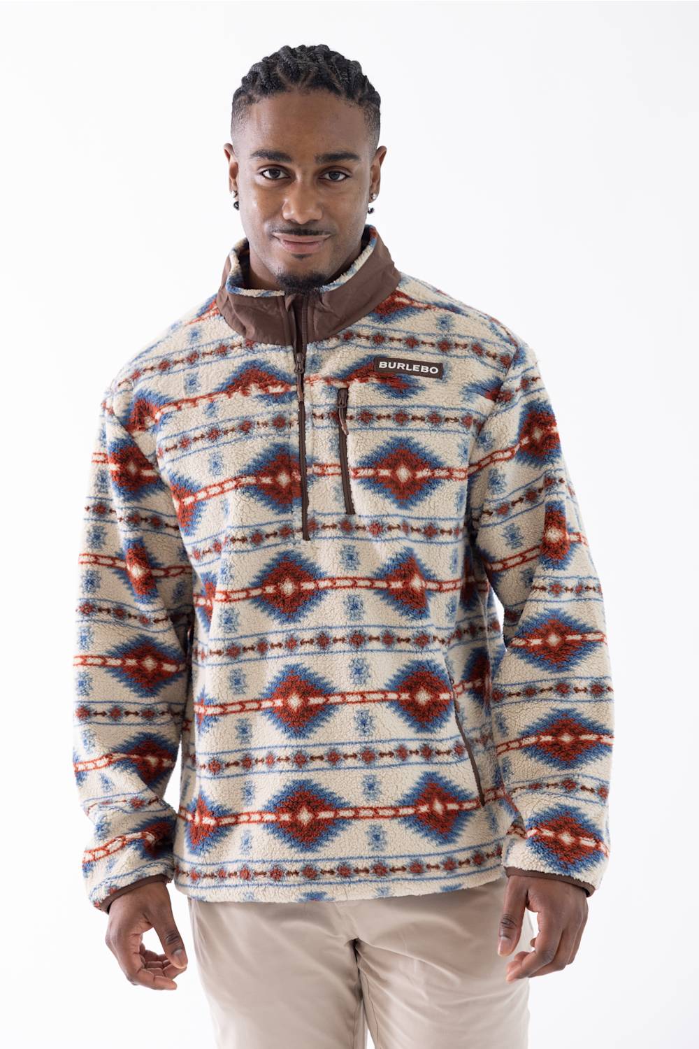 A man wearing a long-sleeve quarter-zip fleece pullover with a Southwestern geometric pattern in red, blue, and beige, paired with beige pants, against a plain white studio background.