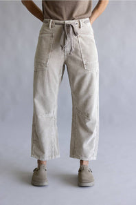 A person wearing light beige wide-leg cropped pants with a drawstring waist, paired with a taupe top and taupe slip-on shoes, shown against a neutral gray studio background.
