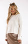 A woman modeling a cream ribbed knit long-sleeve sweater with a brown satin skirt and a brown bow headband, set against a plain white studio background.