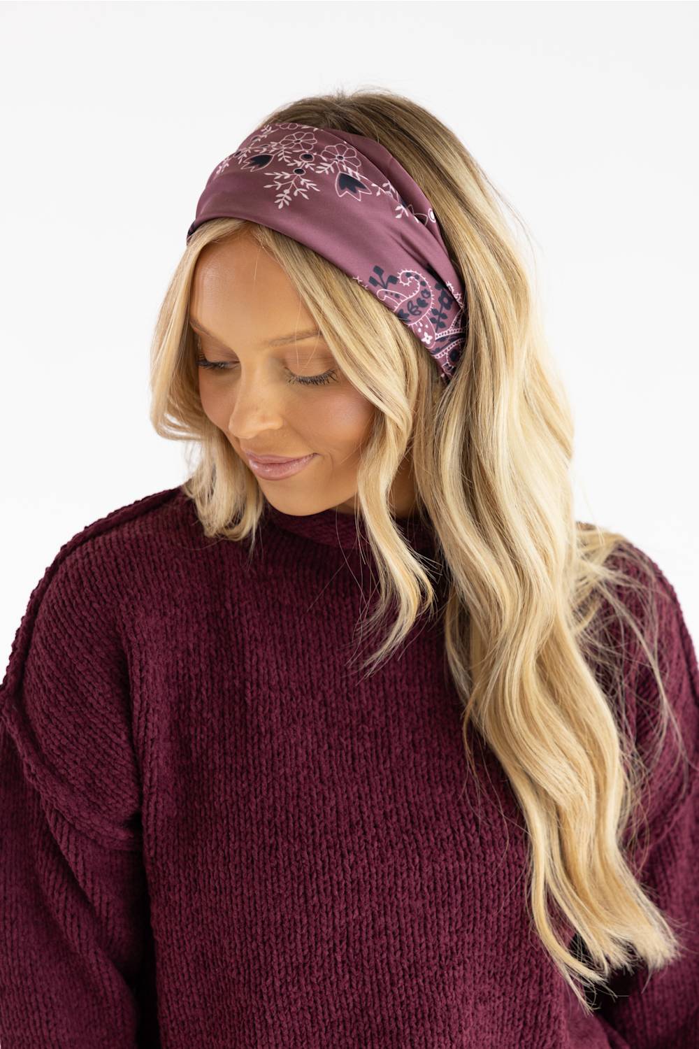 A woman with long blonde hair wearing a mauve paisley bandana headband and a matching mauve knit sweater, shown against a plain white background.