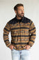 A man wearing a quarter-zip fleece pullover with a Southwestern geometric pattern in brown, tan, black, and orange, paired with light-wash jeans, photographed against a neutral light gray background.