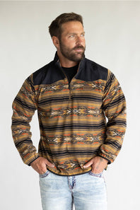 A man wearing a quarter-zip fleece pullover with a Southwestern geometric pattern in brown, tan, black, and orange, paired with light-wash jeans, photographed against a neutral light gray background.