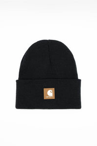A black ribbed knit beanie hat with a folded cuff, featuring a small tan square patch on the front with the Carhartt logo, set against a plain white background.