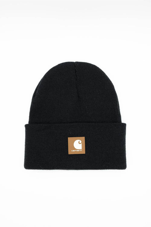 A black ribbed knit beanie hat with a folded cuff, featuring a small tan square patch on the front with the Carhartt logo, set against a plain white background.