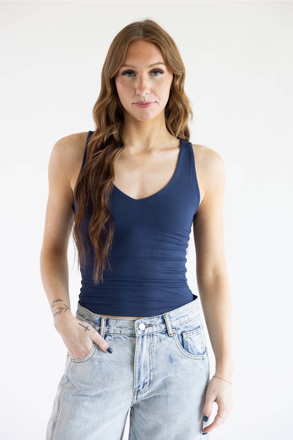A woman modeling a dark navy blue tank top paired with light-wash denim jeans against a plain white studio background.