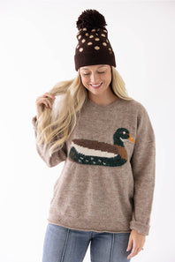 Model wearing a brown and cream polka dot beanie with a fuzzy pom-pom and a cozy beige sweater featuring a mallard duck graphic.