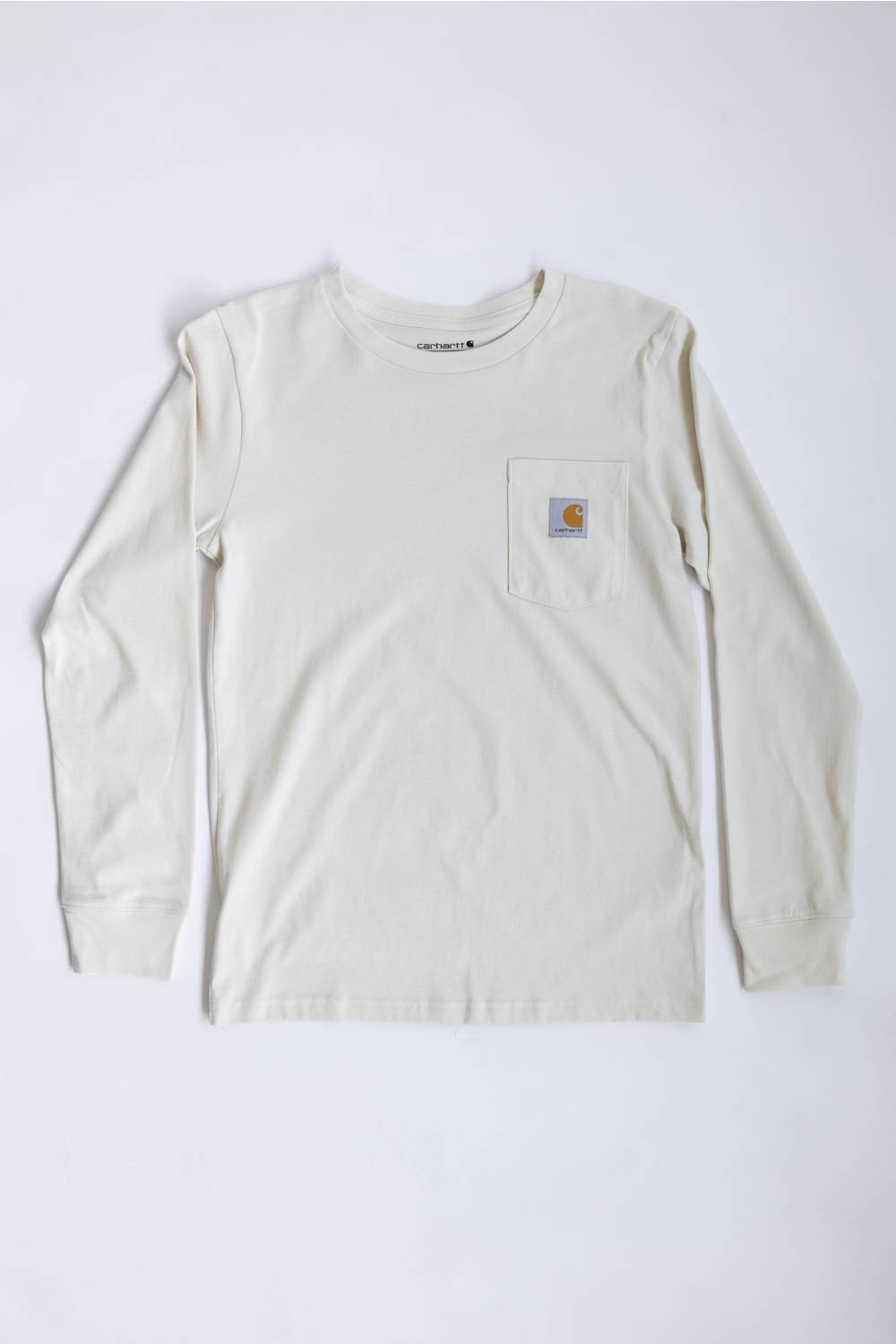 A light cream long-sleeve pocket t-shirt with a classic Carhartt logo patch on the left chest, laid flat against a white background.