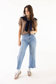 A woman modeling a brown short-sleeve top with a navy blue knit scarf tied around her neck, paired with light-wash wide-leg jeans and beige lace-up shoes, against a plain white studio background.