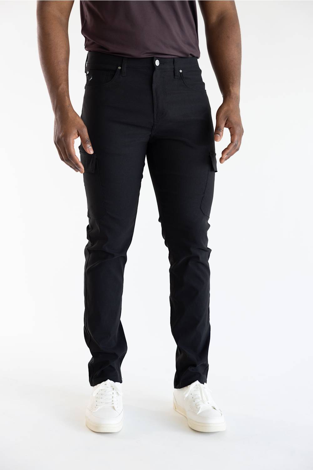 A person wearing slim-fit black cargo-style jeans with white sneakers, shown from the waist down against a clean white studio background.