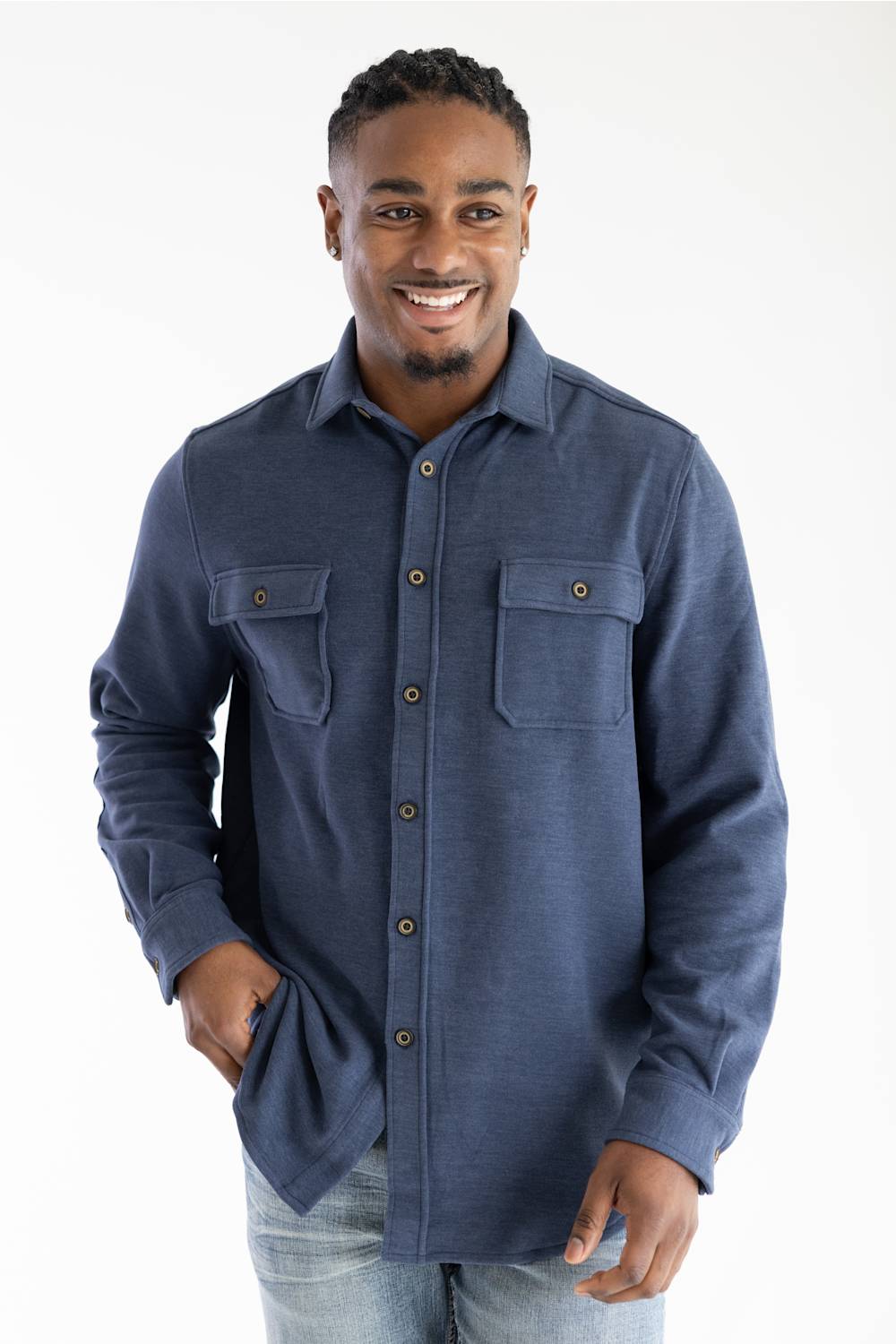 A smiling man wearing a navy blue long-sleeve button-up shirt with two chest pockets and light blue jeans, standing against a plain white studio background.