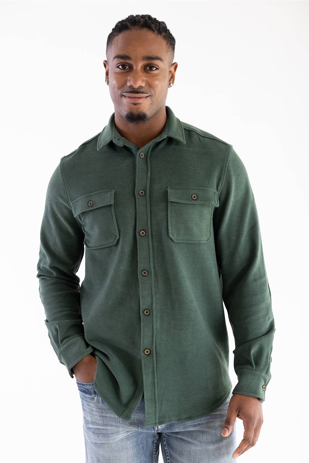 A man wearing a dark green long-sleeve button-up shirt with two chest pockets and light blue jeans, standing against a plain white background.