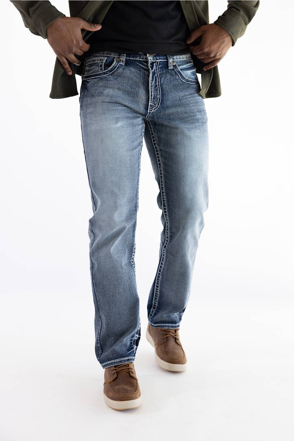 A person wearing light-wash blue denim jeans with a black shirt and olive green jacket, standing against a plain white studio background.
