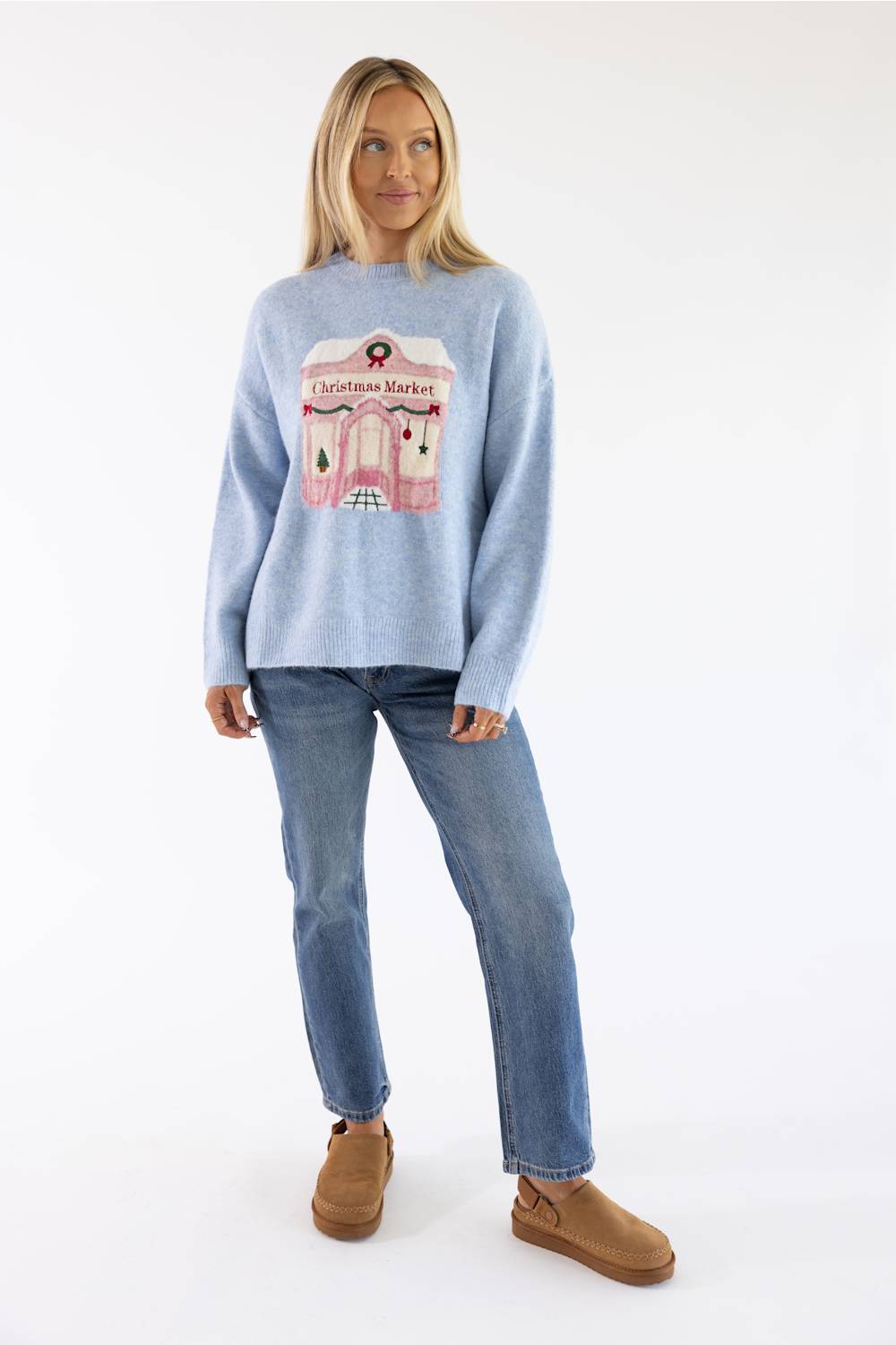 Blonde woman modeling a periwinkle blue christmas market storefront sweater with jeans