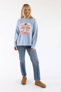 Blonde woman modeling a periwinkle blue christmas market storefront sweater with jeans