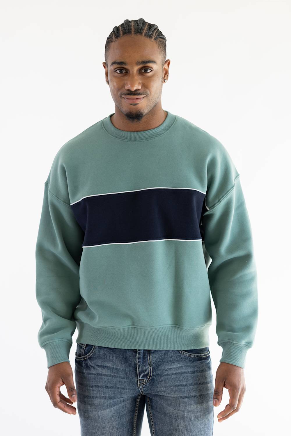 A man wearing a sage green crewneck sweatshirt with a thick navy blue horizontal stripe across the chest, paired with blue jeans, against a plain white background.