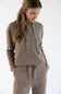 A woman wearing a matching ribbed knit lounge set in sand brown, featuring a hooded sweatshirt with leopard-print drawstrings and coordinating pants, against a plain white background.