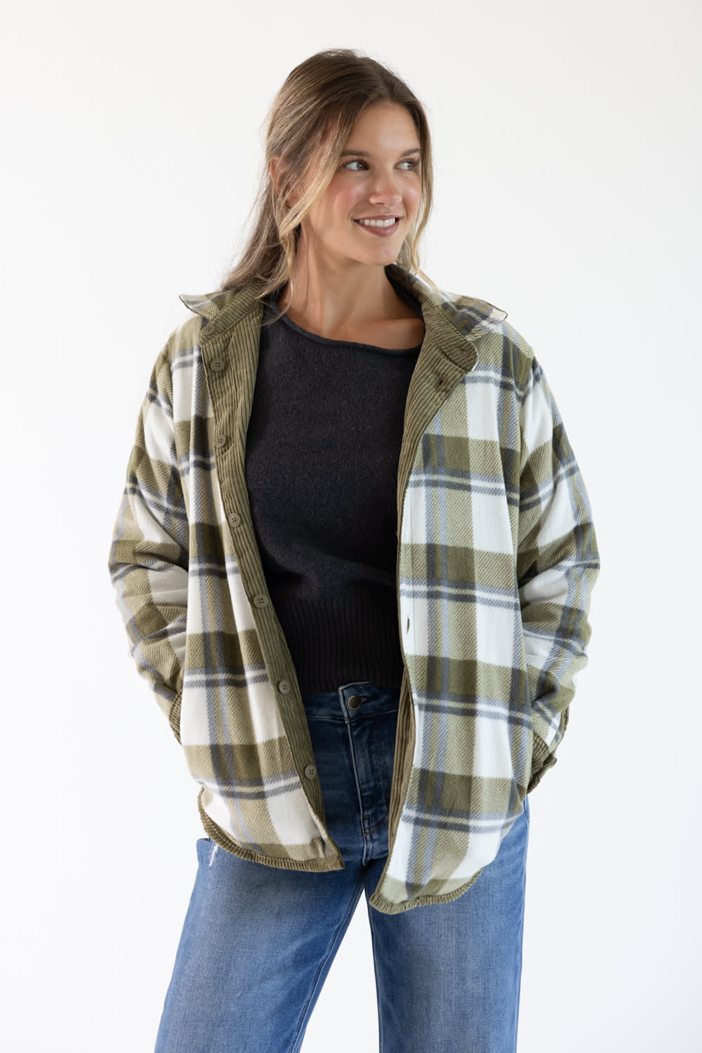 A woman modeling an oversized plaid flannel shirt jacket in olive green, white, and gray, worn open over a black top and blue jeans against a plain white background.
