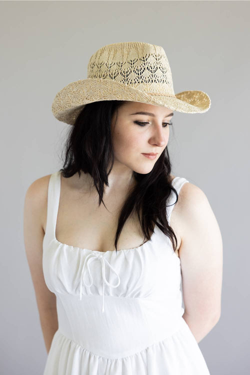 Woman wearing a straw hat with lace details against a plain background