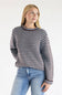 A woman wearing a long-sleeve knit sweater with horizontal brown, black, and light blue stripes, paired with light-wash blue jeans, against a plain white studio background.