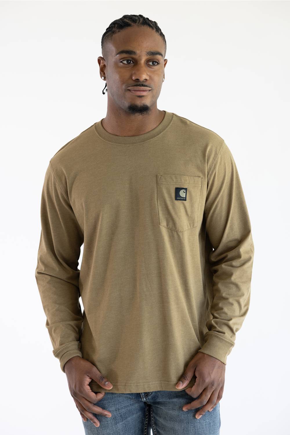 A man wearing a longsleeve light brown t-shirt with a black Carhartt patch on the upper left chest pocket.