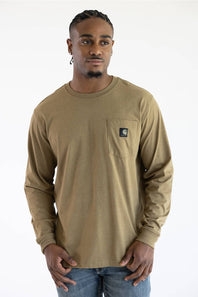 A man wearing a longsleeve light brown t-shirt with a black Carhartt patch on the upper left chest pocket.