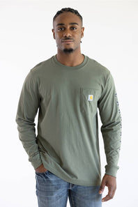 A man wearing the Carhartt Irvine Relaxed Pointer Dog Long Sleeve T-Shirt for Men in Dusty Olive Green featuring a Carhartt logo down the left arm and a classic Carhartt patch logo with front pocket located on the upper left chest.