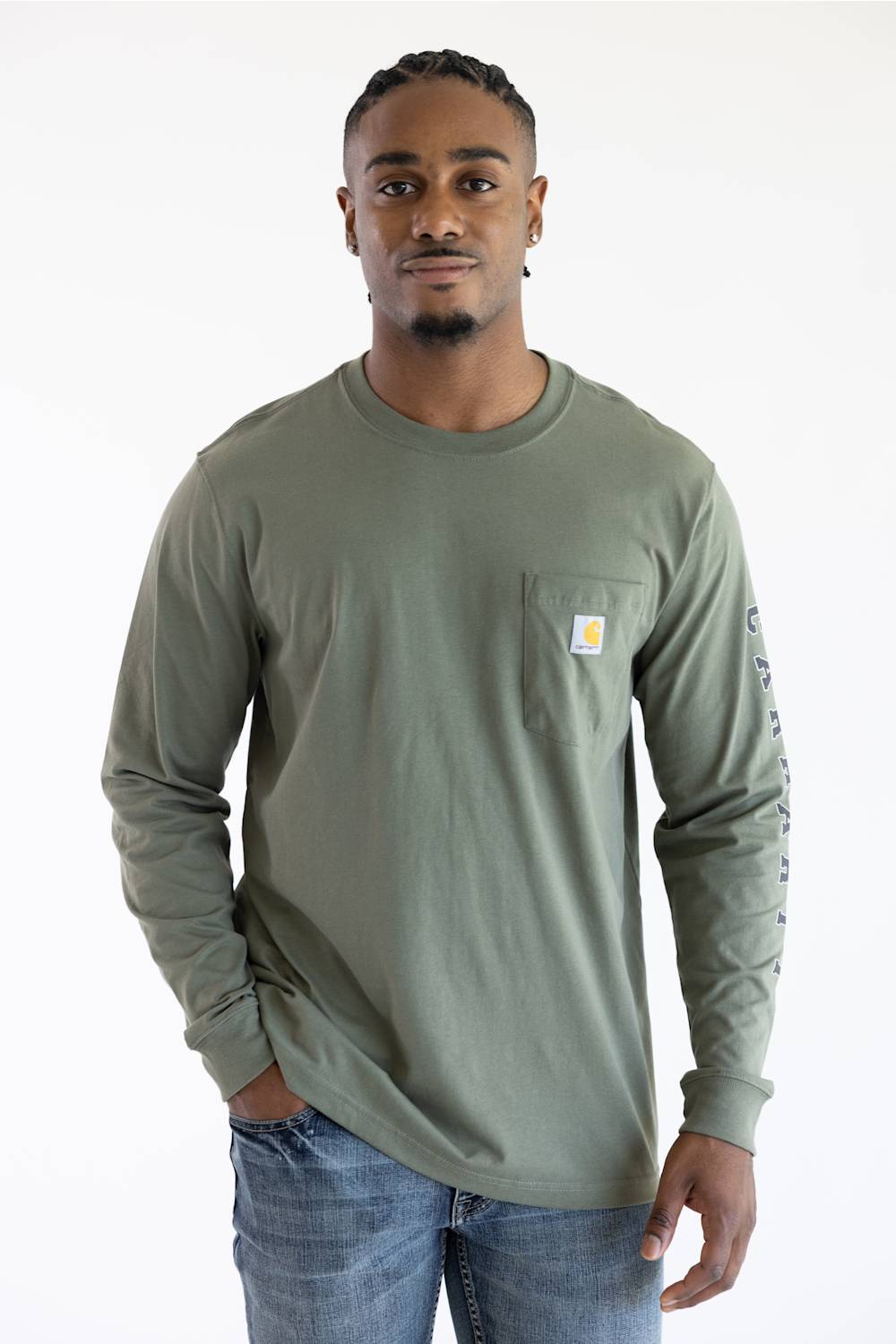 A man wearing the Carhartt Irvine Relaxed Pointer Dog Long Sleeve T-Shirt for Men in Dusty Olive Green featuring a Carhartt logo down the left arm and a classic Carhartt patch logo with front pocket located on the upper left chest.