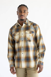 A man wearing a Carhartt long-sleeve plaid button-up shirt in beige, brown, and blue tones, paired with khaki pants, photographed against a plain white studio background.
